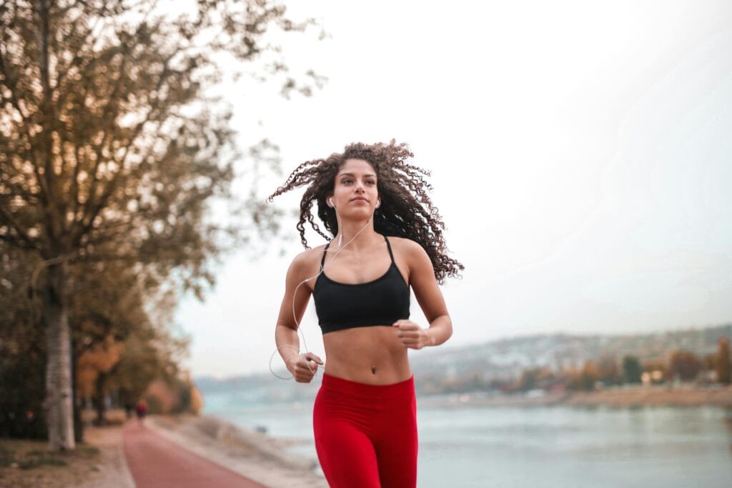 pexels-photo-3764154-3764154 Determined woman in red leggings jogging along a scenic riverside path, embracing fitness outdoors.