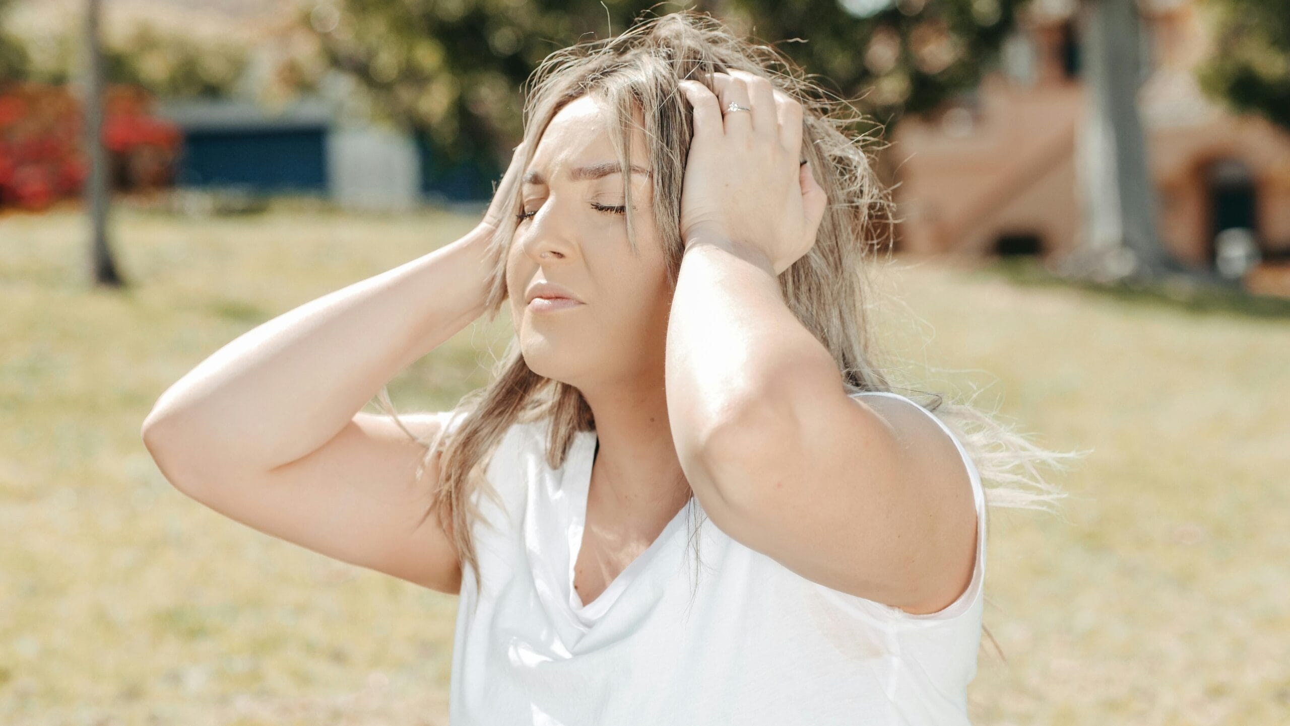 A woman outdoors holding her head, depicting stress and headache.
