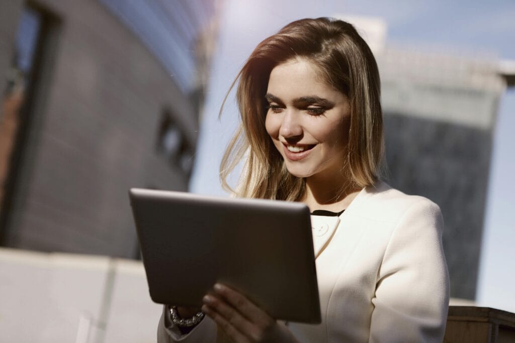 A woman joyfully using a digital tablet outdoors in the city during the day.